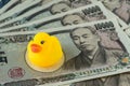 Selective focus on yellow duck doll on pile of japanese yen bank