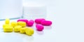 Selective focus on yellow ovoid rectangular tablet pills on blurred background of pink tablet pills and medicine bottle with space