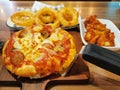 Selective focusing on Pizza serving on wooden plate with onion rings and fries chicken on wooden table