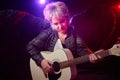 Self-assured adult blonde middle age woman with black angel wings and guitar like a rock musician. Model posing in Royalty Free Stock Photo