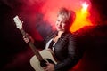 Self-assured adult blonde middle age woman with black angel wings and guitar like a rock musician. Model posing in Royalty Free Stock Photo