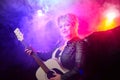 Self-assured adult blonde middle age woman with black angel wings and guitar like a rock musician. Model posing in Royalty Free Stock Photo