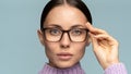 Self-assured confident business woman touches eyeglasses, looking at camera,  on studio blue background Royalty Free Stock Photo