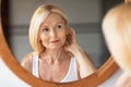 Self-care concept. Attractive middle aged blonde woman looking at mirror, enjoying her reflection and beauty treatments Royalty Free Stock Photo