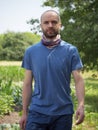 A self-confident bald man with facial hair walks among the plants in summer. A confident, purposeful look. Portrait