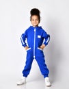 Self-confident dark-skinned kid girl in blue trendy jumpsuit with pockets and zipper stands with her hands in pockets