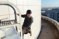 A self-confident industrial climber in gear holds onto a ladder on the roof of an office building