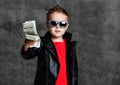 Self-confident rich kid boy in sunglasses, leather jacket and red t-shirt handing us a bundle stack of money cash