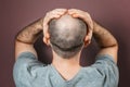 Self-doubt and inferiority complex. Baldy adult man grabs his head with his hands. Rear view. Brown background. The