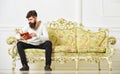 Self education concept. Man with beard and mustache sits on baroque style sofa, holds book, white wall background. Guy