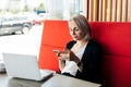 A self-employed woman is working with her phone and laptop on the terrace of a restaurant over a cup Royalty Free Stock Photo