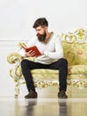 Self improvement concept. Guy reading book with attention. Man with beard and mustache sits on baroque style sofa, holds