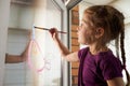 Self-isolation at home. Child quarantined girl paints a rainbow on a glass window. Art Therapy Royalty Free Stock Photo