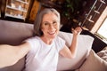 Self-portrait of attractive cheerful grey-haired woman sitting on divan welcoming you at loft industrial home house flat