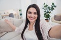 Self-portrait of attractive cheerful hospitable long-haired woman sitting on divan inviting home indoors