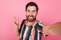 Self portrait of smiling friendly mature man in striped t shirt show v sign recording video greetings isolated on pink Royalty Free Stock Photo