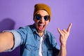 Self portrait of trendy stylish cheerful rude screaming guy taking selfie showing you horned fingers rock sign wearing Royalty Free Stock Photo