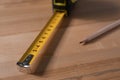 Self retracting metal measuring tape and pencil on wooden table, closeup