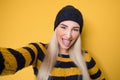 Selfie. Close-up funny mocked woman takes photo of himself with her smartphone while tongue sticking out, model wearing woolen cap Royalty Free Stock Photo