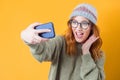 Selfie. Close up girl takes photo of himself with her smartphone, isolated on yellow background