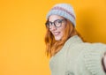 Selfie. Close up pleased beautiful girl takes photo of himself with her smartphone, isolated on yellow background. Focus on face