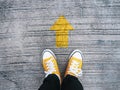 Selfie feet wearing yellow sneakers in front of arrow on concrete road