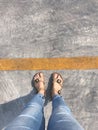 Selfie of female feet wearing brown sandals and blue jeans on the road. Royalty Free Stock Photo