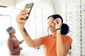 Selfie, optometry and woman trying glasses with prescription lenses and frame in an optical store. Vision, smile and