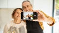 Selfie at romantic dinner. Happy senior couple taking selfie on smartphone in kitchen interior, selective focus Royalty Free Stock Photo