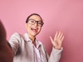 Selfie on smartphone of a stunning Latin American woman smiling and greeting with her hand, isolated on pink background