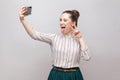 Selfie time! Portrait of happy foolish joyful attractive blogger woman wearing in striped shirt standing, winking and showing