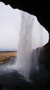 Vertical view of Seljalandsfoss, a great waterfall from the back, behind the waterfall with a cloudy sky
