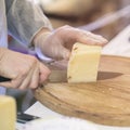 Seller cuts and sells cheese, cut cheese heads on wooden market board. Hands with knife close-up. Selective focus Royalty Free Stock Photo