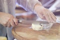 Seller cuts, sells cheese with truffle, cut cheese heads on wooden market board. Hands with knife close-up. Gastronomic Royalty Free Stock Photo
