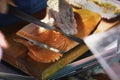 Seller cuts and sells salmon on wooden market board. Hands with knife close-up. Gastronomic fish produce, popular with