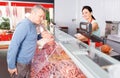 Seller helping male choosing sausages in shop