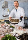 Seller holds basket of small mussels standing near a counter