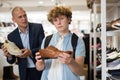 Seller offers various shoes to a teenager in shoe store