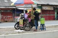 a seller of sugar cane juice drinks serving a customer on the side of the main road close to the city park