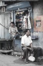 The seller of a window-sized convenience store waits for customers in a street of Kolkata, India. Another man sits by on a stool