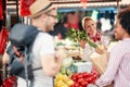 Seller woman offers fresh and organic vegetables at the green market or farmers market stall.  Young buyers choose and buy Royalty Free Stock Photo