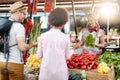 Seller woman offers fresh and organic vegetables at the green market or farmers market stall.  Young buyers choose and buy Royalty Free Stock Photo