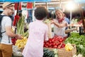 Seller woman offers fresh and organic vegetables at the green market or farmers market stall.  Young buyers choose and buy Royalty Free Stock Photo