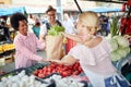 Seller woman selling fresh and organic vegetables at the green market or farmers market stall.  Young buyers choose and buy Royalty Free Stock Photo