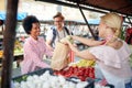 Seller woman selling fresh and organic vegetables at the green market or farmers market stall.  Young buyers choose and buy Royalty Free Stock Photo