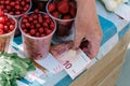 Selling berries at the farmers' market. Cherries and strawberries in plastic glasses. Elderly woman's hand
