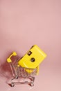 Selling and buying photo equipment.Yellow camera in a basket against a pink background. Creative, a place for text.