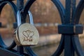 Semi-circular shiny golden-silver padlock engraved with two woven hearts fixed on round elements of bridge fence.