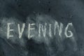 Semi-erased word EVENING on black chalkboard. Handwritten word. Fuzzy letters on black surface. The concept of changing the time