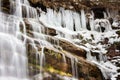 Semi-frozen colorful Tupavica waterfall close up and sunlit red rocks and yellow grass